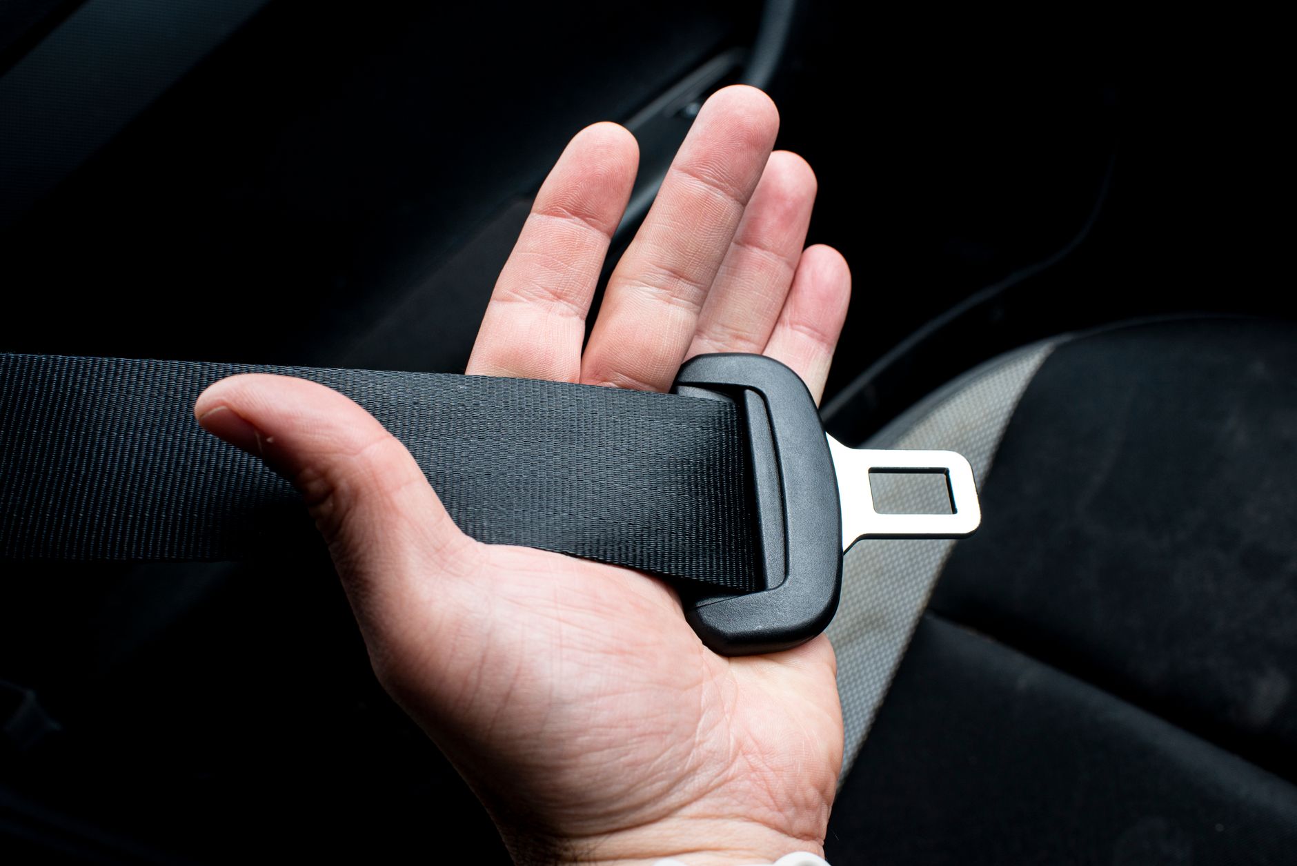 person buckling seatbelt around cat carrier on car floor between front and back seats